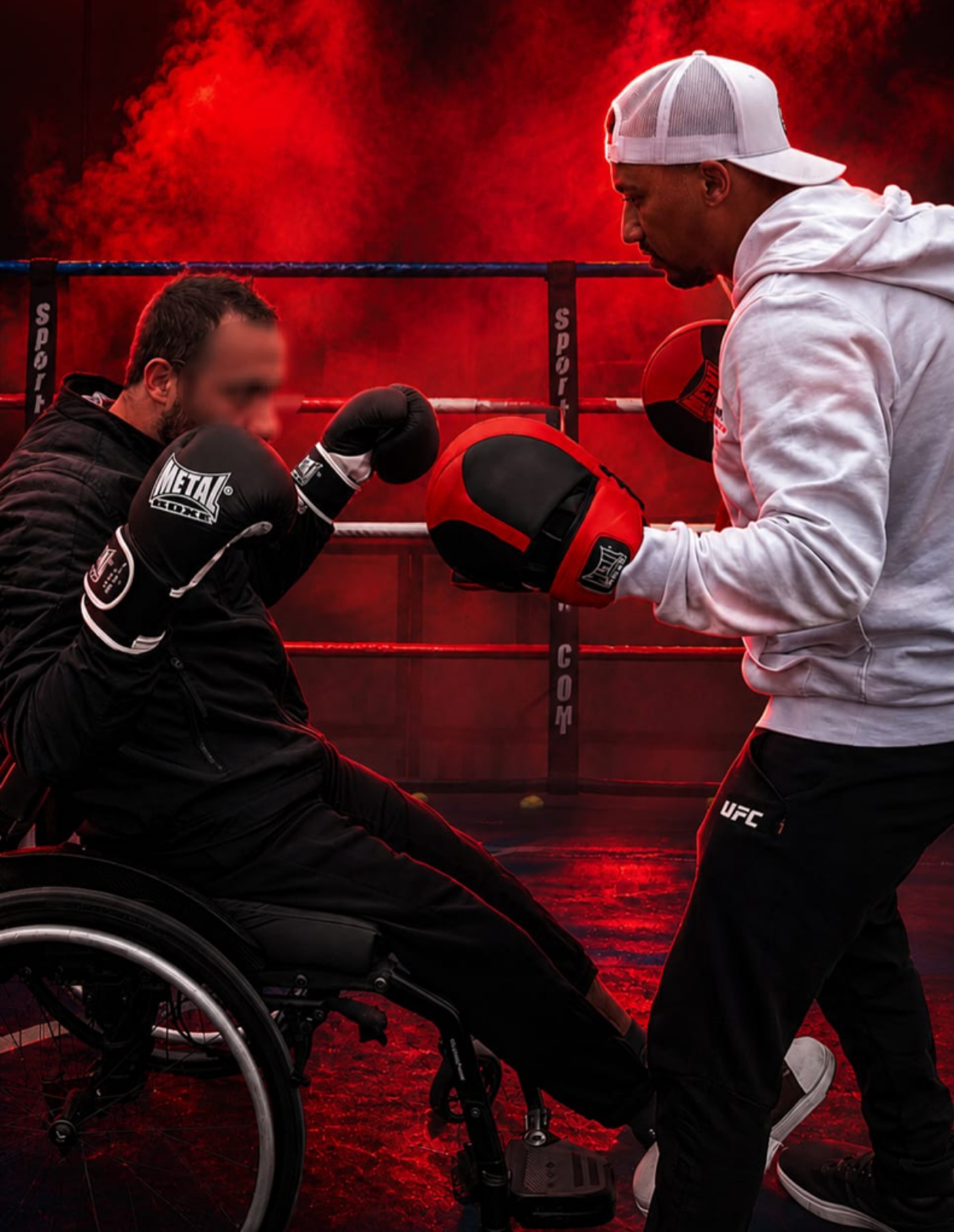 Photo d'un boxeur en fauteuil roulant frappant des pattes d'ours tenues par son coach, sur le ring